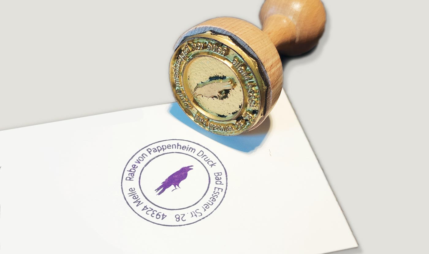 Runder Stempel liegend von unten gesehen, daneben ein Papier mit dem aufgedruckten Stempelabdruck