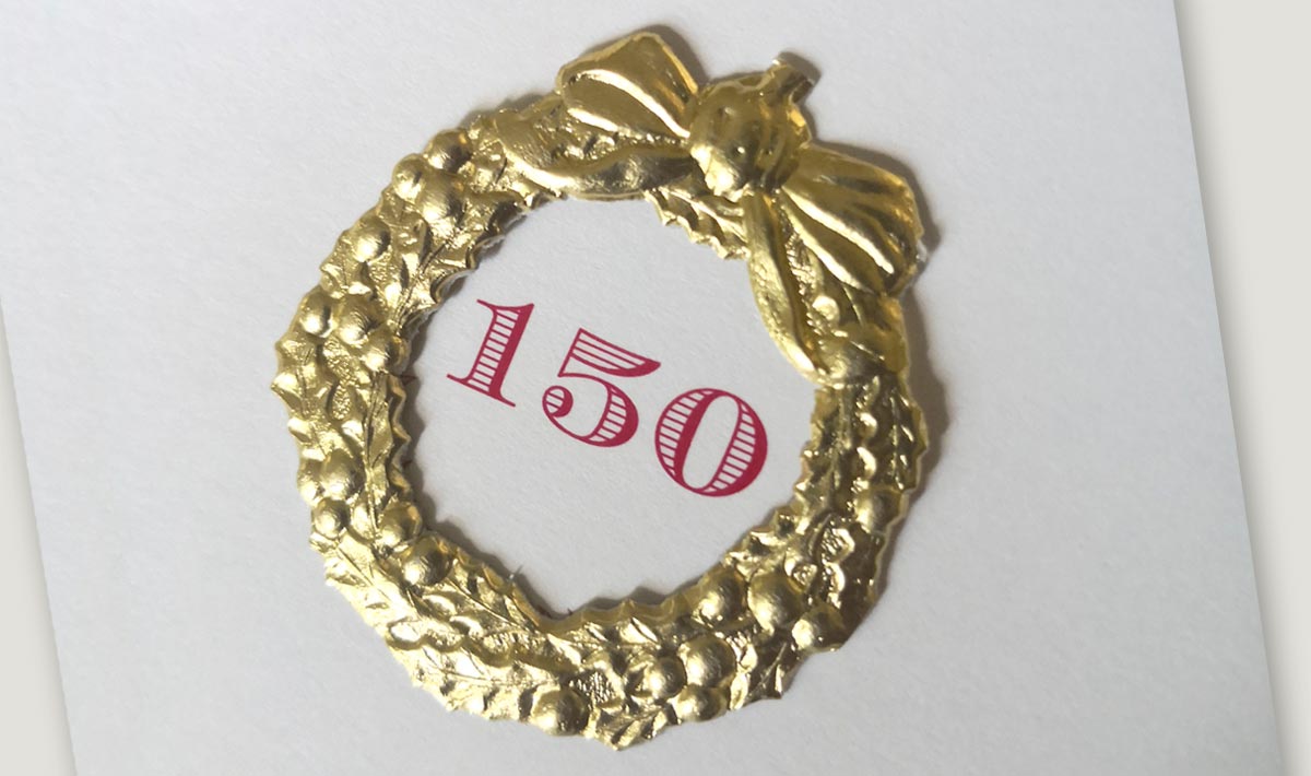 Karte mit goldfarbenem Dresdner Pappen-Kranz und Schleife, mittig aufgeklebt.